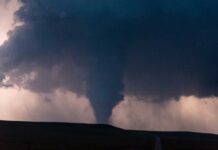A tornado forming under dark storm clouds with lightning in the background