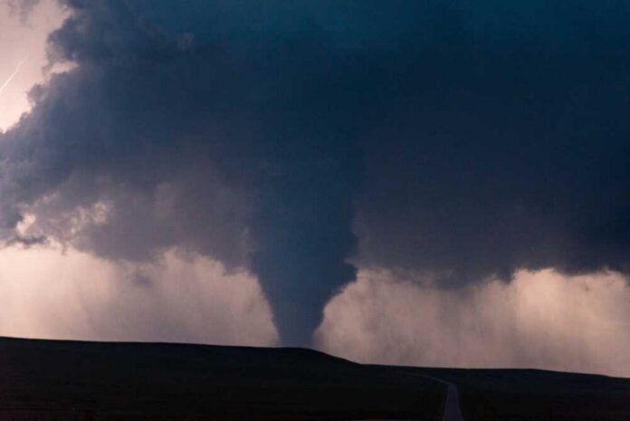 A tornado forming under dark storm clouds with lightning in the background