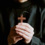 A person holding a wooden cross pendant