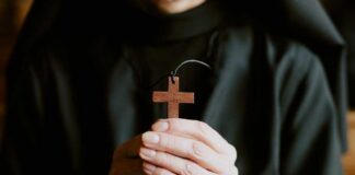 A person holding a wooden cross pendant