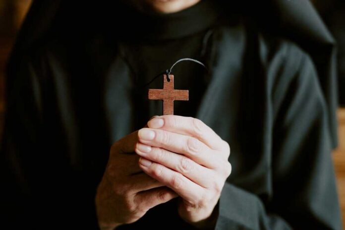 A person holding a wooden cross pendant