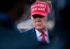 A political figure wearing a red hat with a serious expression