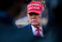 A political figure wearing a red hat with a serious expression