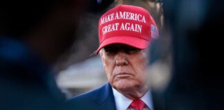 A political figure wearing a red hat with a serious expression