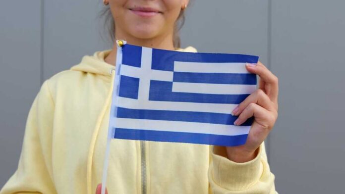 shutterstock_2607305489.jpg Young woman holding a small Greek flag