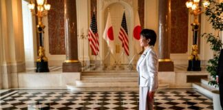 A woman in formal attire standing in a grand hall with flags in the background