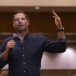 A speaker gesturing while holding a microphone during a presentation