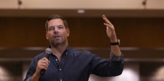 A speaker gesturing while holding a microphone during a presentation