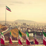 ABRUPT Reversal Leaves Iranian Diplomats Stranded View of Iranian flags with a city and mountains in the background