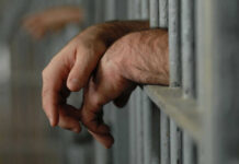Hands resting on jail cell bars.