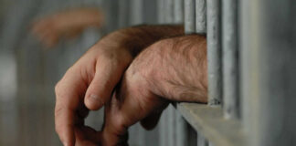 Hands resting on jail cell bars.