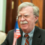 Bolton SLAMS Trump’s Diplomacy — Iran Talks ‘Waste of Oxygen’ Man with glasses smiling near small American flag