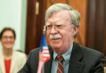 Bolton SLAMS Trump’s Diplomacy — Iran Talks ‘Waste of Oxygen’ Man with glasses smiling near small American flag