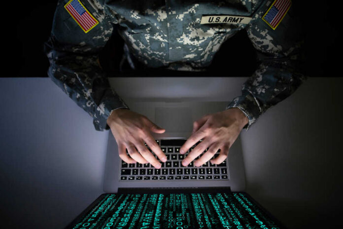 American,Soldier,In,Military,Uniform,Preventing,Cyber,Attack,In,Military A soldier in U.S. Army uniform typing on a laptop with green code displayed on the screen