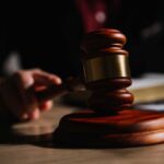 A wooden gavel resting on a table with a blurred hand in the background