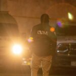 A law enforcement officer standing in front of police vehicles at night
