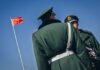 Ping-Pong Parlor Hid SHOCKING Spy Operation Two Chinese soldiers in uniform standing near the national flag