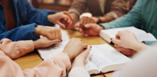 Group of hands holding each other over an open Bible