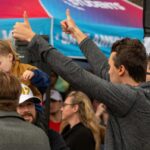 A man giving a thumbs up while holding a child at a lively outdoor event