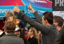 A man giving a thumbs up while holding a child at a lively outdoor event