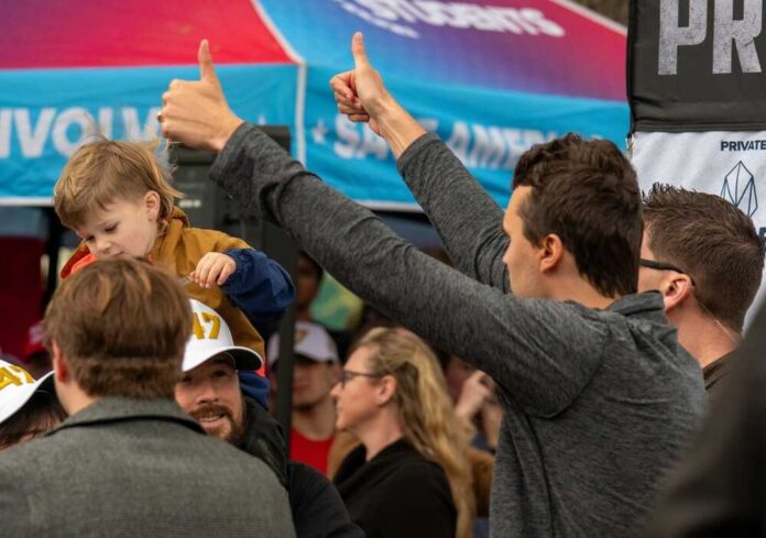 A man giving a thumbs up while holding a child at a lively outdoor event