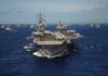 SUSPICIOUS Timing: Allies Deploy After US Sacrificed An aircraft carrier surrounded by various naval vessels in the ocean