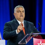Man in suit speaking at a podium on a stage