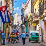 Socialism Crashes — Cuba Scrambles For Cash Colorful street scene with Cuban flag and people.