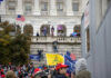 Encrypted Clues Tease J6 Bombshells Crowd with flags at U.S. Capitol building.