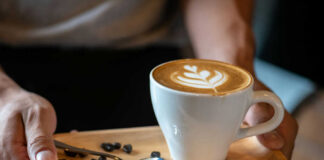 Latte with latte art on a wooden tray with coffee beans and a spoon