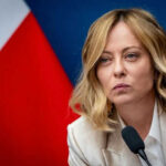 Diplomatic Meltdown Over One Photo Person speaking at a conference with flag background