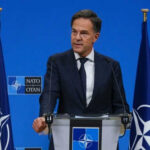Trump Squeezes NATO — 5% Or Else? Man speaking at podium with NATO flags behind him