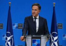 Man speaking at podium with NATO flags behind him
