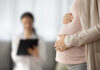 Pregnant person holding their belly during a medical visit