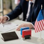 Shock Push: Deport Naturalized Terrorists A professional reviewing documents with stamps and an American flag on the table