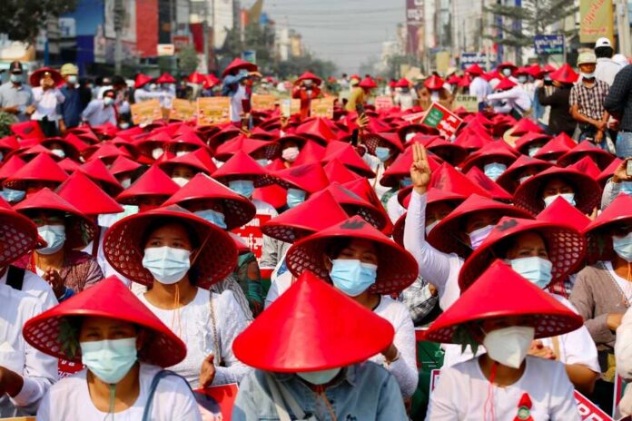 Protest,In,Mandalay,myanmar:people,Of,Myanmar,Protest,Calling,For,Freedom,And A view of destroyed buildings with smoke rising in the background