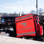 A motorcycle with a bright red Doordash delivery bag parked in an urban area