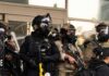 Police officers in tactical gear wear gas masks during a crowd control operation