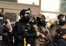 Police officers in tactical gear wear gas masks during a crowd control operation