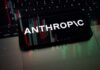 Commerce Clampdown Freezes Anthropic Globally Smartphone displaying the word 'ANTHROPIC' over a background of financial graphs