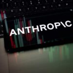 Commerce Clampdown Freezes Anthropic Globally Smartphone displaying the word 'ANTHROPIC' over a background of financial graphs