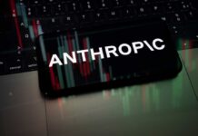 Commerce Clampdown Freezes Anthropic Globally Smartphone displaying the word 'ANTHROPIC' over a background of financial graphs