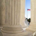 Marble columns of a neoclassical building with U.S. flag in background