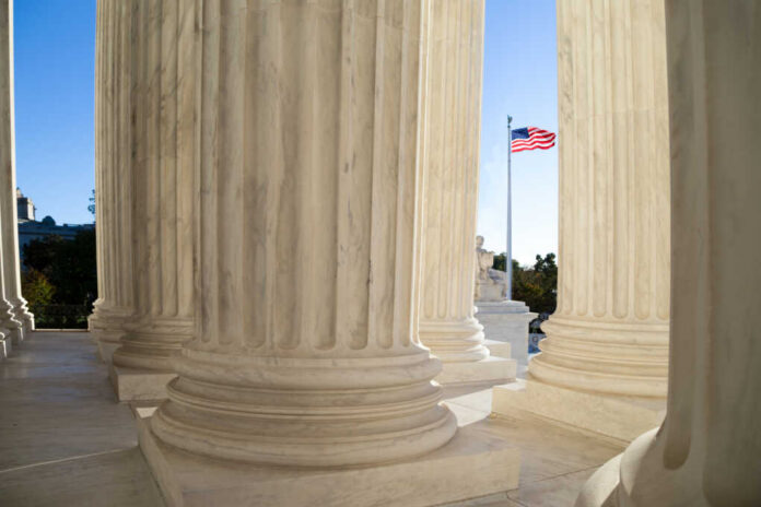 Front,Terrace,Of,The,Supreme,Court,Of,U.s. Marble columns of a neoclassical building with U.S. flag in background