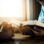 Two individuals engaged in prayer with a Bible