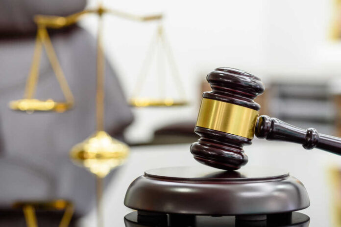 A wooden gavel resting on a sound block with a blurred scale of justice in the background