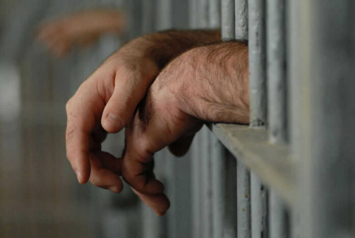 Hands resting on jail cell bars.