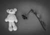 Crocheted bear and wilted rose on gray background