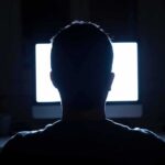 person silhouetted in front of a bright computer screen