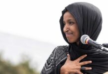 Woman in black hijab speaking at a microphone outdoors